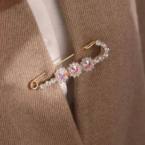 Crystal safety pin brooch detail, elegant gold-tone metal flower pin for apparel.