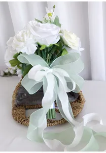 Detailansicht eines weißen künstlichen Brautstraußes mit grün-weißen Schleifen für die Hochzeit.