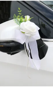 Detailed close-up of a white artificial wedding car mirror flower with bow and green leaves.