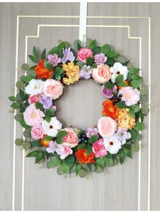 Close-up detail of colorful artificial floral wreath with vibrant peonies and green leaves hanging.