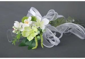 Künstliche Hochzeits-Trinkglas-Blumendekoration mit weißem Band und grünen Blättern.