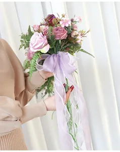 Wundersamer künstlicher Kaskaden Brautstrauß mit lila Rosen und fließenden Bändern für Hochzeit.