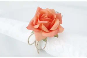 Primo piano dettagliato di portatovagliolo con rosa artificiale pesca e corda di juta.