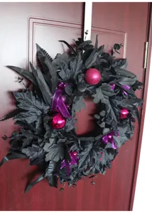 Black artificial Halloween wreath detail, featuring maple leaves and purple ribbons for door decor.