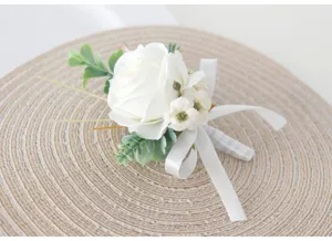 Close up of white artificial rose boutonniere with green leaves and ribbon detail.