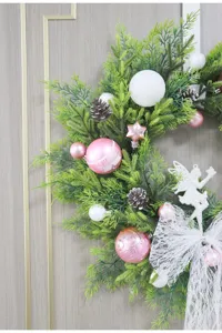 Corona de Navidad rosa con bolas blancas, piñas, lazo y ángel para decoración de puerta festiva.