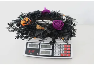 Halloween zwarte krans detailweergave met paarse roos en pompoen op digitale weegschaal.
