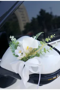 Detail view of artificial calla lily wedding car decoration flower with white bow and green leaves.