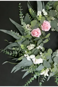 Detailaufnahme eines künstlichen Blumenkranzes mit rosa Rosen und Eukalyptus für Heimdekoration.