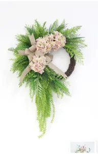Detail view of artificial hydrangea wreath with green leaves and burlap bow for home decor.