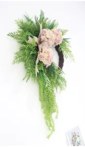 Close-up of artificial green fern wreath with pink hydrangeas and rustic bow decor.