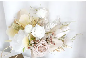 Nahaufnahme des künstlichen Brautstraußes mit weißen Rosen, Champagnerrosen und Goldblättern.