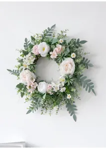 Detalle exquisito de la corona de flores artificiales con rosas rosas y hojas verdes.