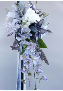 Primo piano di bouquet da sposa artificiale a cascata con gigli viola e dettagli di nastri.