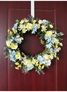 Spring floral wreath detail, artificial yellow and blue flowers hanging on wooden door decor.