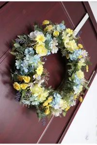 Detail view of spring artificial flower wreath with yellow and blue blooms for home door wall decor