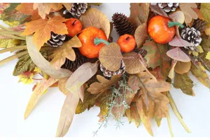 Autumn Thanksgiving wreath detail shot featuring artificial maple leaves, pinecones, and pumpkins.