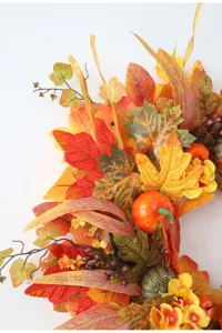 Detailed close-up shot of artificial autumn maple leaves, pumpkins and berries wreath decor.