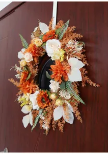 Close up detail of artificial autumn wreath featuring orange flowers and foliage for decor.