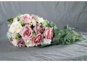 Detail view of artificial cascading bridal bouquet with pink and white roses and green leaves.