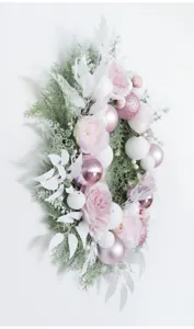 Close up of pink and white Christmas wreath with floral and decorative baubles for wall.