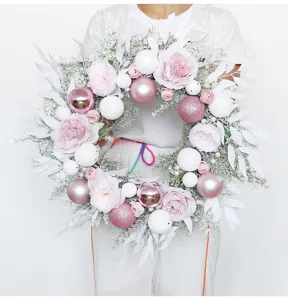 Pink Christmas wreath detail showcasing frosted leaves, pink roses and decorative baubles.