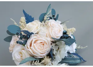 Squisito bouquet da sposa artificiale con rose champagne e dettaglio di fogliame blu.