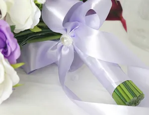 Primer plano del mango del ramo de novia en cinta de raso morado claro con broche de perlas.
