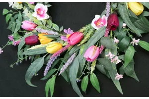 Nahaufnahme des künstlichen Frühlingskranzes mit bunten Tulpen, Orchideen und grünen Blättern.