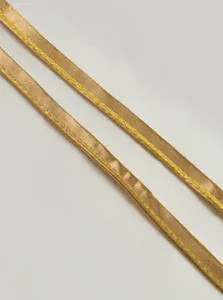 Close up detail of shiny gold ribbon strap with yellow stitching, clothing accessory.