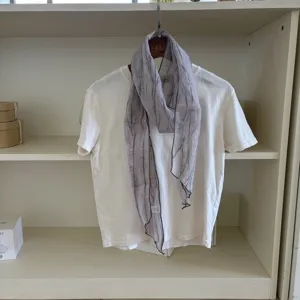 Detailed view of the retro grey narrow linen scarf draped on a white tee inside a neat shelf.