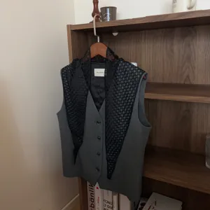 Detailed view of grey suit vest layered with black lace floral triangle scarf, stylish outfit.