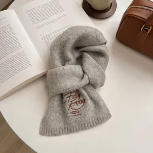 Grey knit scarf detail, cozy winter neck warmer with brown embroidery, soft wool texture close-up