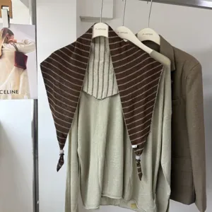 Detail shot of a chic striped triangular scarf layered with knit top on hanger in a stylish showroom setup.