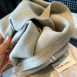 Detailed view of a light blue wool scarf featuring contrast yellow stitching and soft texture.