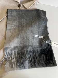 Close-up detail of grey plaid wool scarf featuring soft fringe and 100% wool material.