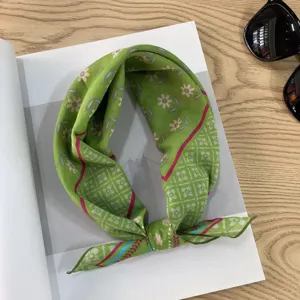 Detailed closeup of a green vintage floral patterned square scarf styled neatly on a wooden desk.