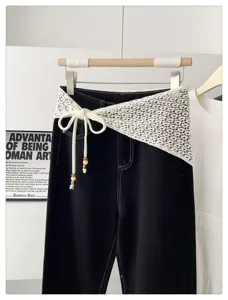 Detail view of black denim pants paired with white crochet knit asymmetric wrap belt and beads.