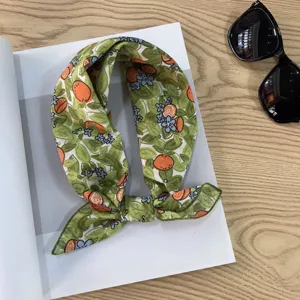 Detailed close-up of the green citrus and floral print scarf displayed on a wooden table.