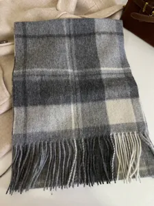Grey plaid wool scarf detail showing soft fabric texture and classic fringed tassels.