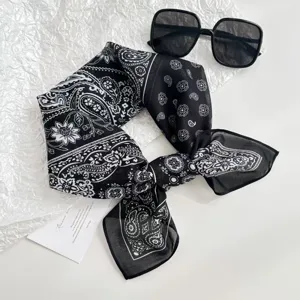Black and white paisley pattern square scarf detail view with stylish sunglasses flat lay.