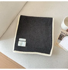 Detailed view of the dark grey knit scarf with white trim and stylish fabric labels for winter.