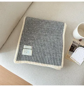 Close-up of grey knitted scarf with white trim detail, cozy texture on sofa background view.