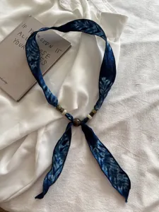 Blauwe tie-dye stoffen lintketting met delicate kralen, vintage literaire stijl detail.
