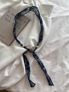 Close-up detail van donkerblauwe bloemige stoffen lintketting met vintage kraalaccenten voor dames.