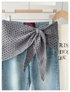 Detail shot of hollow-out knit shawl scarf draped on denim jeans, versatile sun protection.