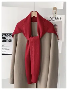 Detail shot of a red cable knit scarf shawl layered over a beige coat for autumn winter fashion.