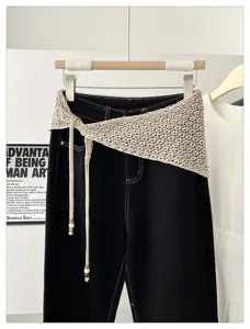 Detail view of a hollow knit crochet triangle scarf draped over black jeans with beaded ties.