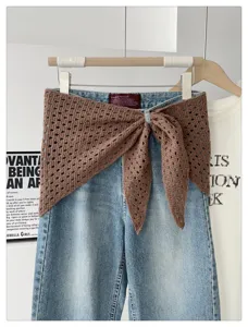 Detail shot of light wash denim jeans paired with a brown hollow-out knit shawl.