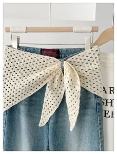 Close-up detail of denim waistband with hollow-out knit wrap bow tie, stylish fashion accessory.